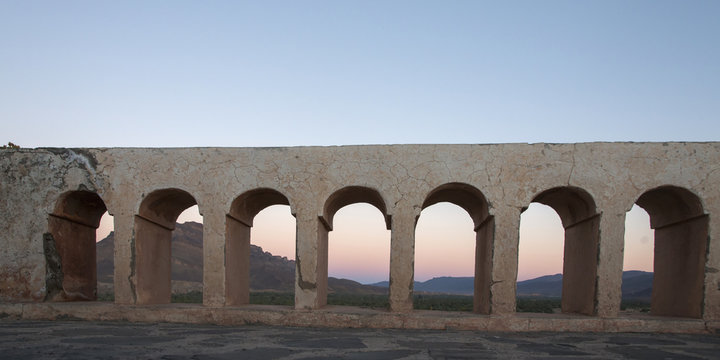 A structure with arches in a row and hills in the background at sunset