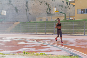 Woman runner jogging on wet red run lane at stadium. 