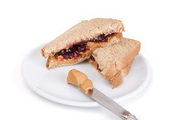 Peanut Butter and Jelly Sandwich – A peanut butter and grape jelly sandwich. On a white plate, on a white background. Knife with peanut butter in the foreground.