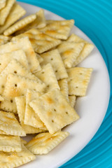Plate of Saltine Crackers – A plate of small saltine crackers. On a white plate with blue background.