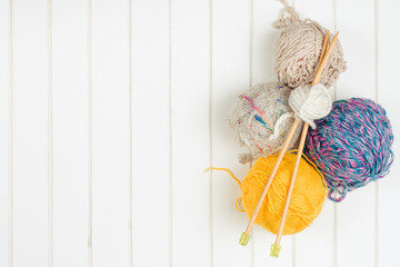 Knitting yarn balls and needles on white wooden background.