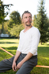 Obraz premium portrait of man sitting on slackline and balancing on a rope