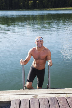 Man getting out of the water onto a dock; Morbylanga, Sweden