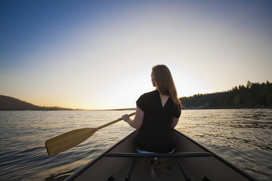 A young woman canoeing at sunset; Vancouver, British Columbia, Canada