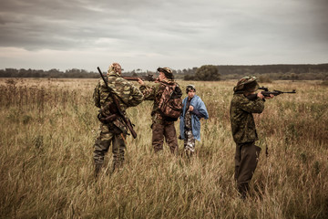 Hunting scene with hunters aiming during hunting season in rural field in overcast day with moody sky 
