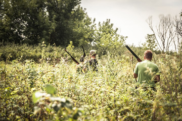 Hunters breaking through bushes during hunting season in summer day