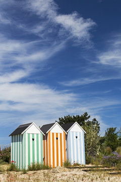 Three colourful striped painted outhouses on a sandy grassy hill with trees; Roscoff, Brittany, France