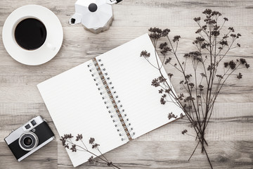 Open scrapbook with pen, coffee and vintage camera on wooden desk with dried flowers.