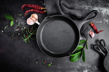 cast iron pan and spices on black metal culinary background, view from above