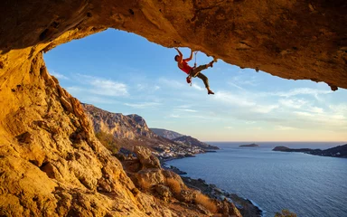 Gordijnen Male climber on overhanging rock against beautiful view of coast below  © Andrey Bandurenko