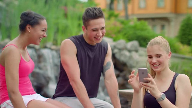 Multiracial people having fun using phone in park. Young friends laughing together. Happy friends watching photos on smart phone. Friendship concept. Young people laughing. People phone. Friends phone