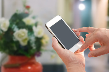 Hand holding mobile smart phone with blank screen in vertical position, blurred people background - mockup template