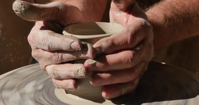 A closeup shot of a craftsman working on a spinning pottery wheel.  	