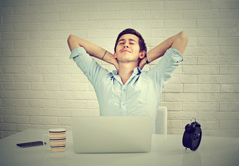 Relaxed man with laptop sitting at desk brick wall background