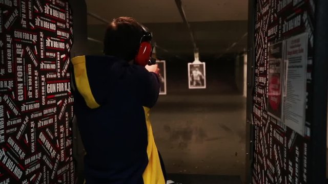 Indoor gun range, male fires hand gun at target, medium shot.