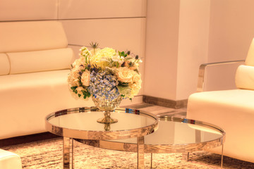 Wedding bouquet in a silver vase on a mirror table with white chairs and a sofa in the background. 