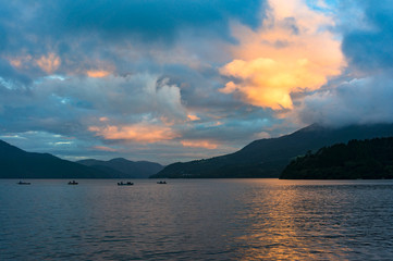 Mountain lake on sunrise with fishing boats in the distance