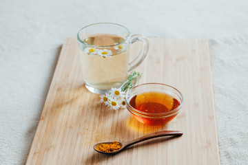 Herbal tea in glass cup with flowers of chamomile, turmeric and honey on a wooden board. Treatment of hot drink. Treatment of folk remedies in bed.
