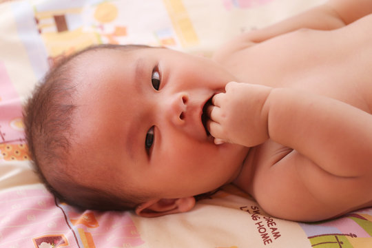 Asian baby smiling happily and have hand sucking on bed.