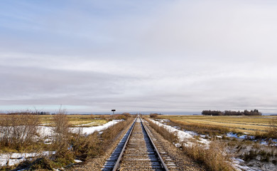Fototapeta na wymiar Railway track dividing harvested fields running straight into the far distance in a barren rural landscape in late autumn