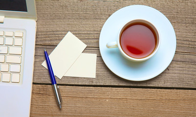 Obraz na płótnie Canvas Blank business cards with pen, laptop and tea cup on wooden office table