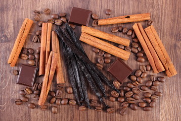 Vanilla, cinnamon sticks, chocolate and coffee grains on wooden surface
