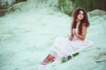 Mysterious woman with long dark hair sits on white sand