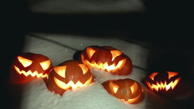 Halloween pumpkins in the winter snowy night with overflying ghost. Looped