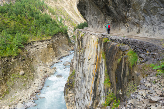 Trekker with backpack walking on trail with beautiful rocks and mountain river. Travel concept. Focus on woman.