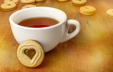 Cup of tea with heart-shaped cookie on blurred background