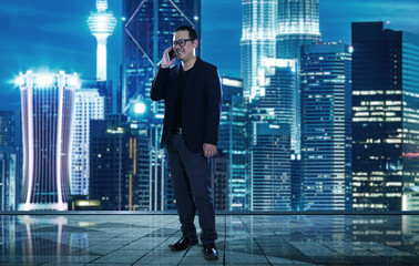 Happy smiling businessman wearing black suit and using modern smartphone near office , successful employer to make a deal while standing near skyscraper office at night.