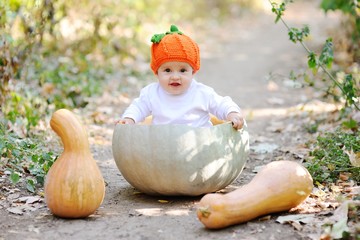 baby girl in the orange cap in the form of a pumpkin sitting inside a huge pumpkin on a background autumn forest. Celebrating Halloween