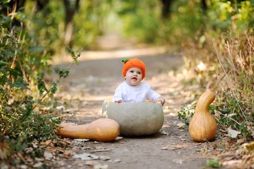 baby girl in the orange cap in the form of a pumpkin sitting inside a huge pumpkin on a background autumn forest. Celebrating Halloween