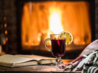 Hot mulled wine and a book on the wooden table. Fireplace with w
