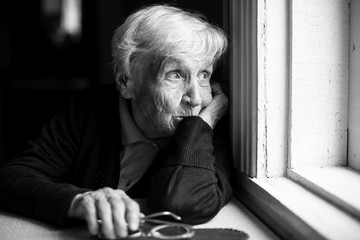 An elderly woman sadly looking out the window, a black-and-white photo. - Powered by Adobe