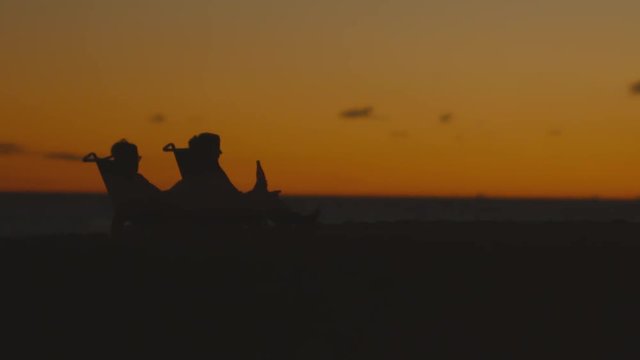 Silhouette of a couple sitting on the beach, watching the ocean at sunset.