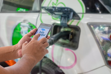 Mobile payment, Cashless society concept. Man using smart phone with NFC tag on screen in electric vehicle station.