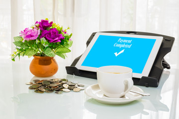Obraz na płótnie Canvas Mobile and Messenging application payment concept. Cup of coffee, money coins, flower pot and digital tablet with payment completed message on screen.