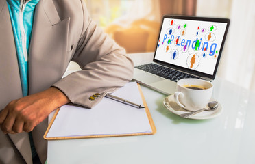 P2P lending concept.  Business man place his hand on blank paper on the table with pen, cup of coffee and laptop computer with P2P lending icons and message on screen.