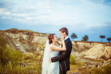 Bride strokes groom's kiss while they pose beneath the hill