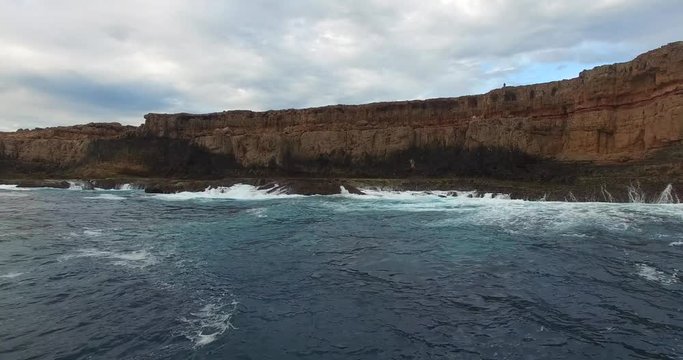 Forward low level aerial fight of big swells breaking against a rugged cliffs at Shark Bay in Western Australia