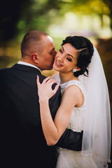 Kissing bride and groom in their wedding day near autumn tree in the forest
