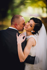 Kissing bride and groom in their wedding day near autumn tree