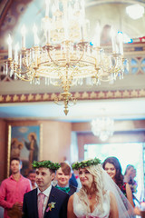 Rich golden chandelier hangs over the newlyweds in green wreathe