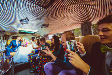 Bride and groom kiss while sitting in the limousine with friends
