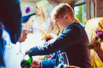 Obraz premium Groomsman pours champagne in the glass while sitting in limousin