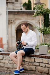 Obraz premium Young photographer with laptopon stone bench andtaking photo on camera