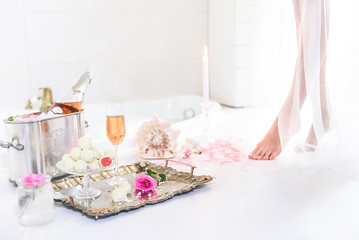 elegant and gentle female legs stepping carefully to the place with champagne, sweets, roses and seashells, white light