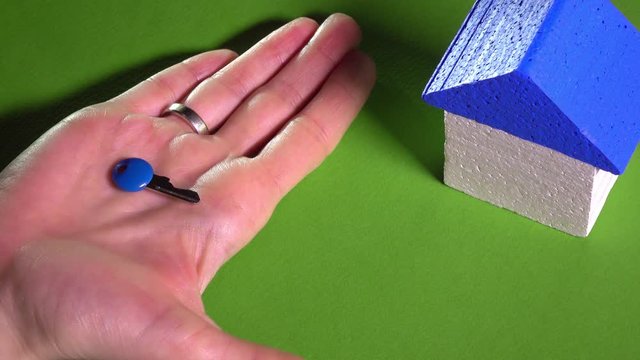 Realtor placing toy house with blue roof and holding small key against green background. Real estate market concept. 4K video