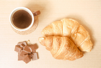 Two baked croissants with a cup of coffee and chocolate.
